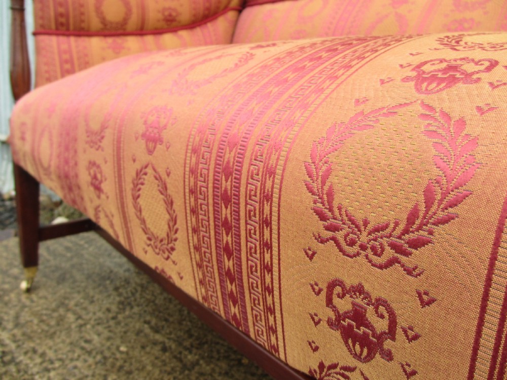 A Regency mahogany framed sofa upholstered in patterned red and gold fabric with reeded legs and brass castors. View IX