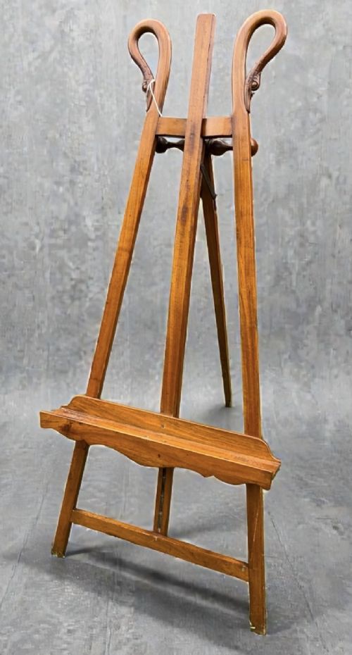 A tall warm brown wooden floor-standing tripod easel featuring carved swan head finials at the top arch and a wide horizontal support shelf. View II