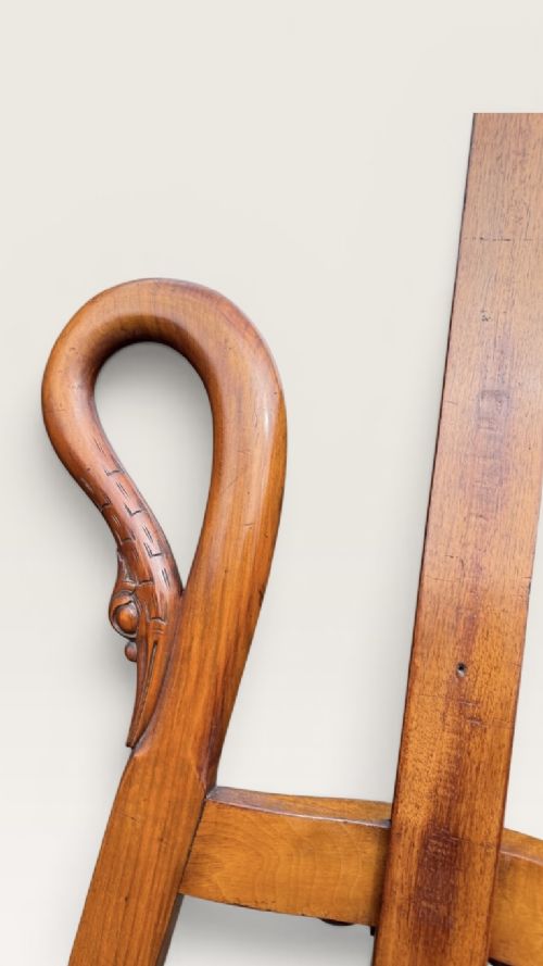 A tall warm brown wooden floor-standing tripod easel featuring carved swan head finials at the top arch and a wide horizontal support shelf. View V