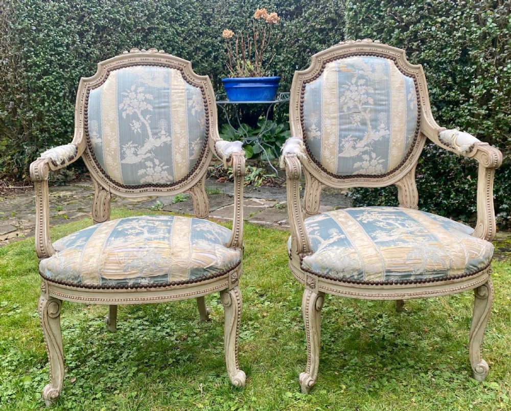 A pair of French style carved armchairs with distressed grey painted wooden frames and blue and cream patterned fabric upholstery.