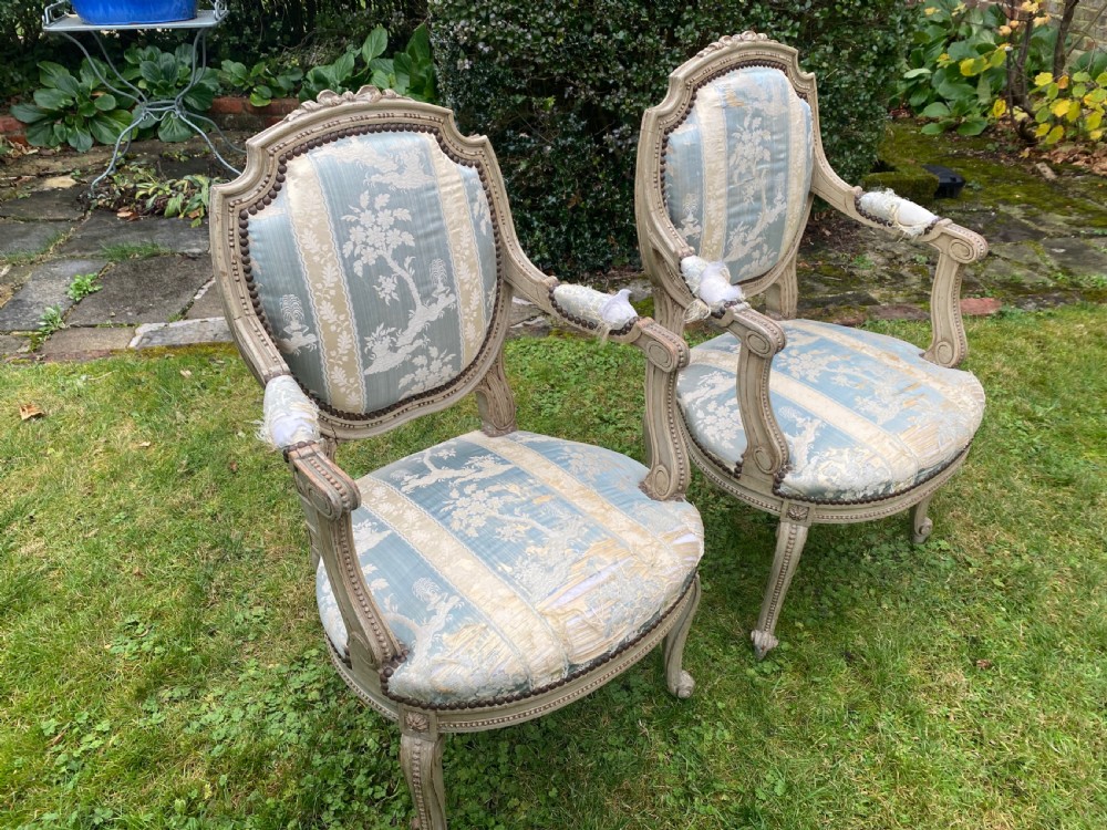 A pair of French style carved armchairs with distressed grey painted wooden frames and blue and cream patterned fabric upholstery. View II