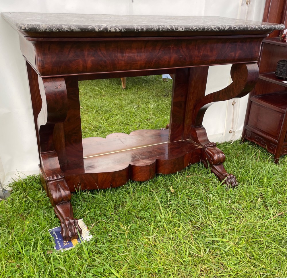 A 19th-century French Louis Philippe console table with flame mahogany veneer, a grey marble top, scrolled front supports, carved claw feet, and a mirrored back.