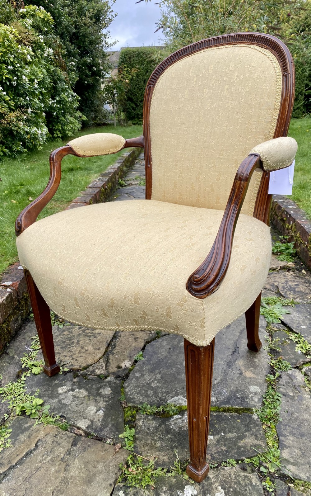 An 18th-century Hepplewhite style open armchair with a carved mahogany frame, padded armrests, fluted front legs, and textured cream fabric upholstery. View IV