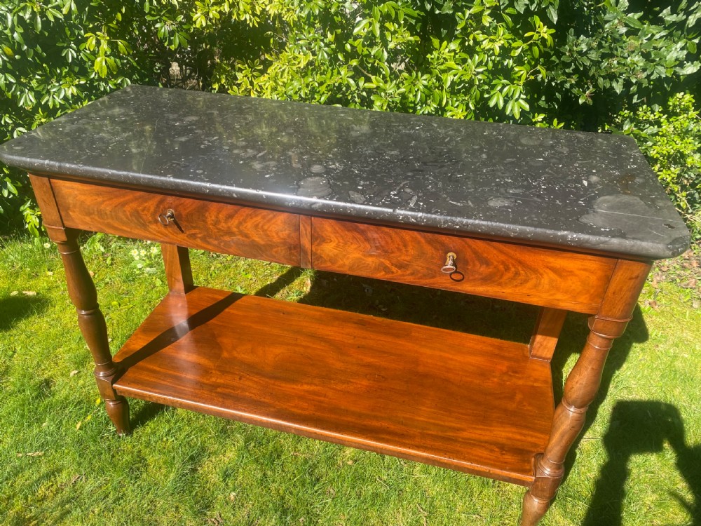 A flame mahogany console table featuring a dark grey marble slab top, two frieze drawers with brass keyholes, turned front supports, and a low undertier shelf. View II