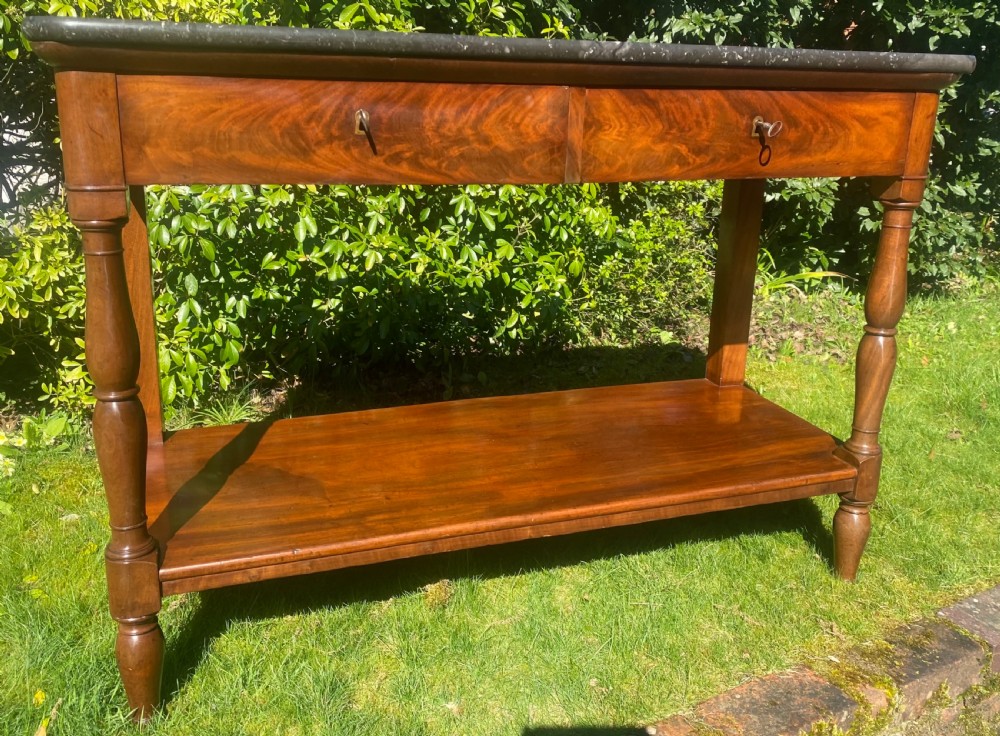 A flame mahogany console table featuring a dark grey marble slab top, two frieze drawers with brass keyholes, turned front supports, and a low undertier shelf. View III