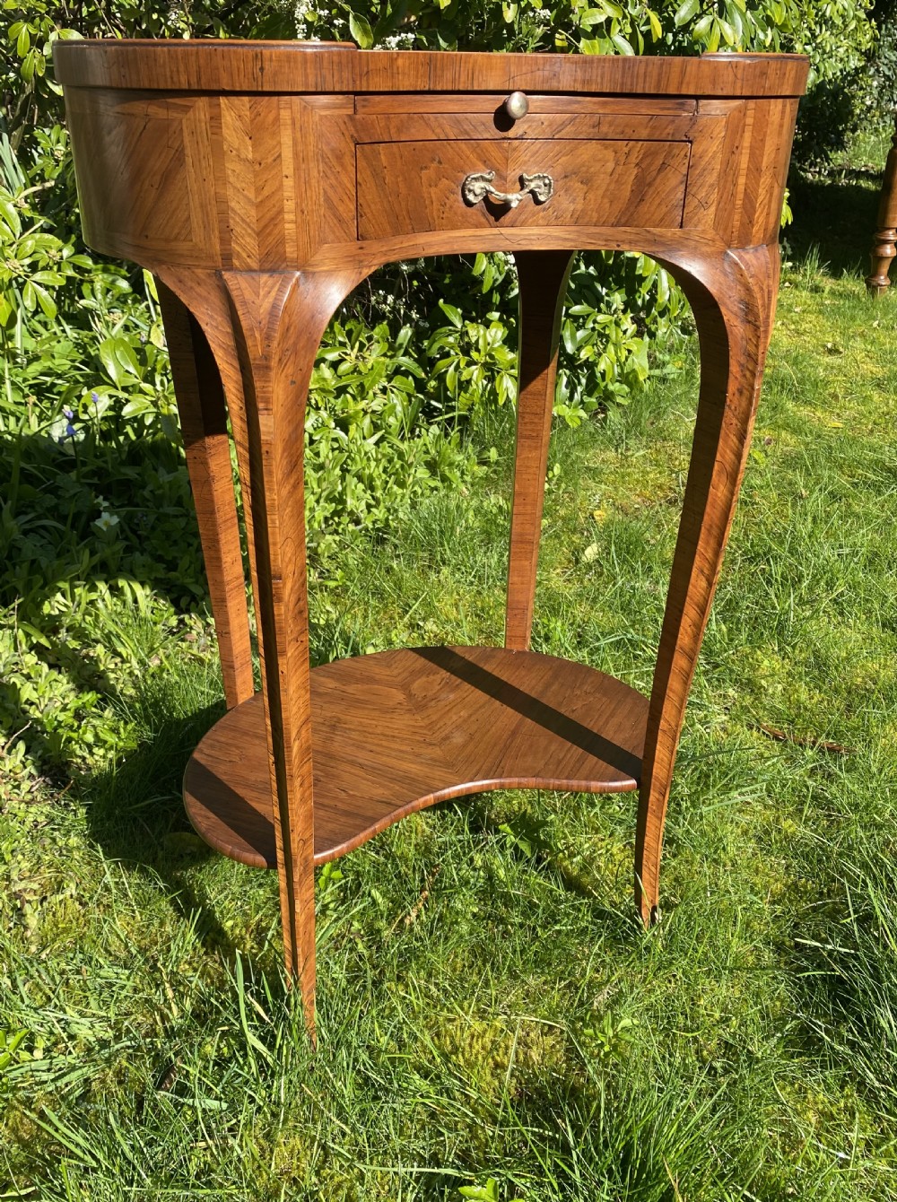 A kidney-shaped wood side table with chevron parquetry veneer, a single drawer with a brass handle, and an undertier shelf. View V