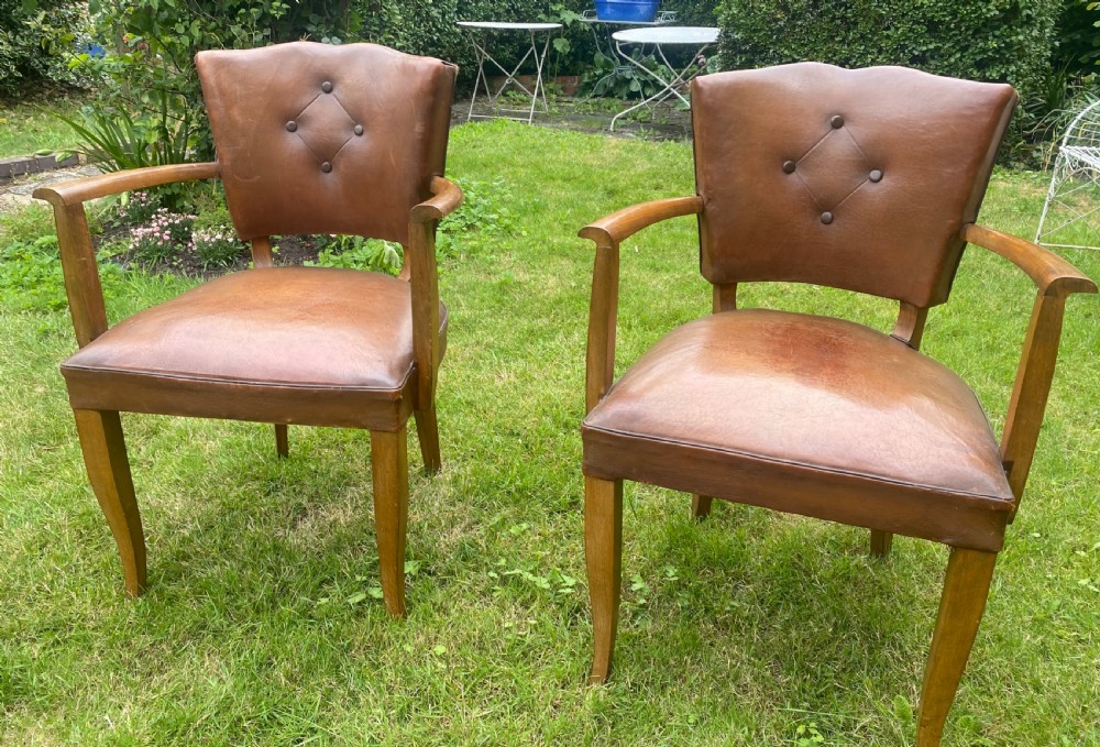 A pair of French Art Deco bridge armchairs with tan brown leather upholstery, diamond button-tufted backrests, and wooden frames.