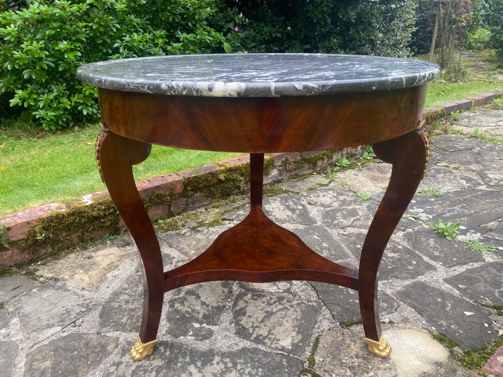 A French Restauration period mahogany gueridon table featuring a circular grey marble top, three curved legs with gilt bronze mounts, and a lower triangular stretcher. View III
