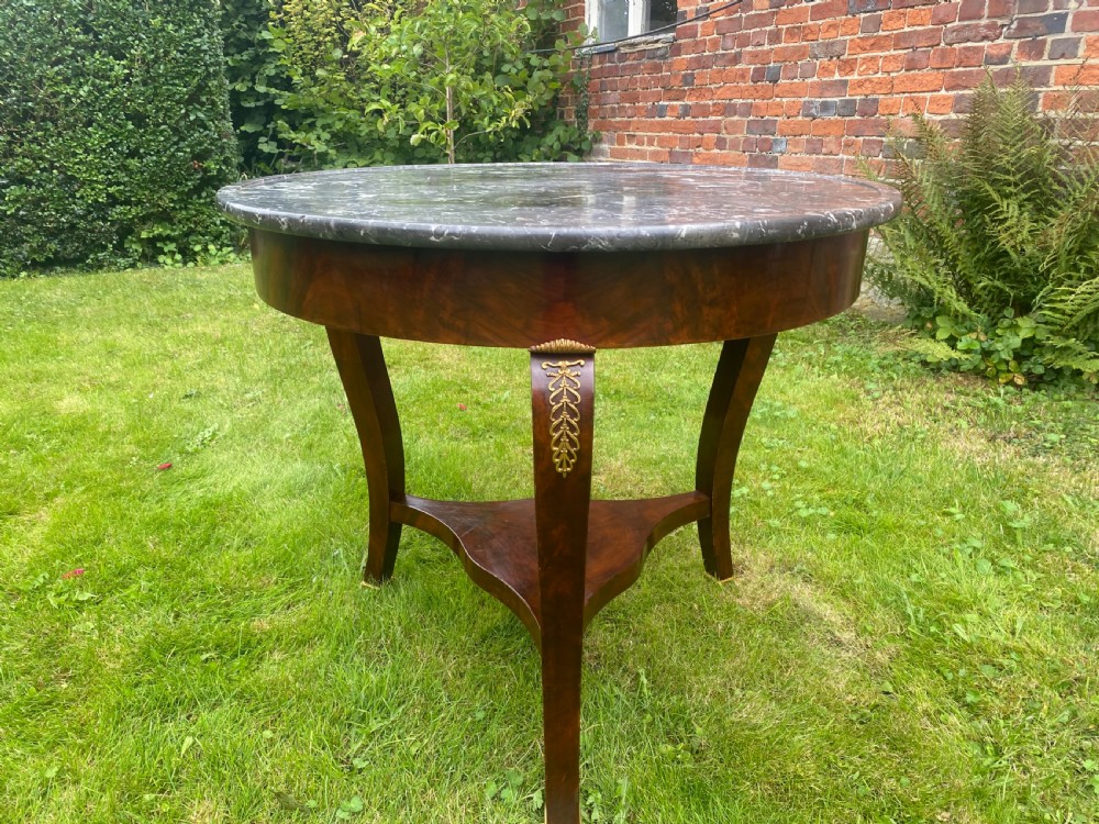 A French Restauration period mahogany gueridon table featuring a circular grey marble top, three curved legs with gilt bronze mounts, and a lower triangular stretcher. View VI
