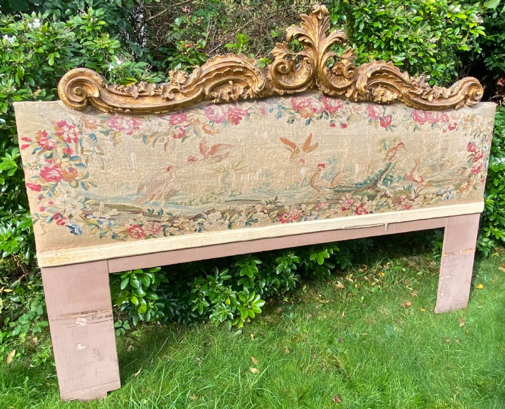 An expansive Venetian style headboard featuring a pictorial woven floral tapestry panel topped with an elaborately carved giltwood cresting.
