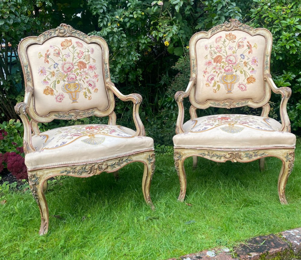 A pair of Italian Rococo style armchairs featuring cream-painted carved wooden frames and floral needlework upholstery depicting urns filled with flowers. View V