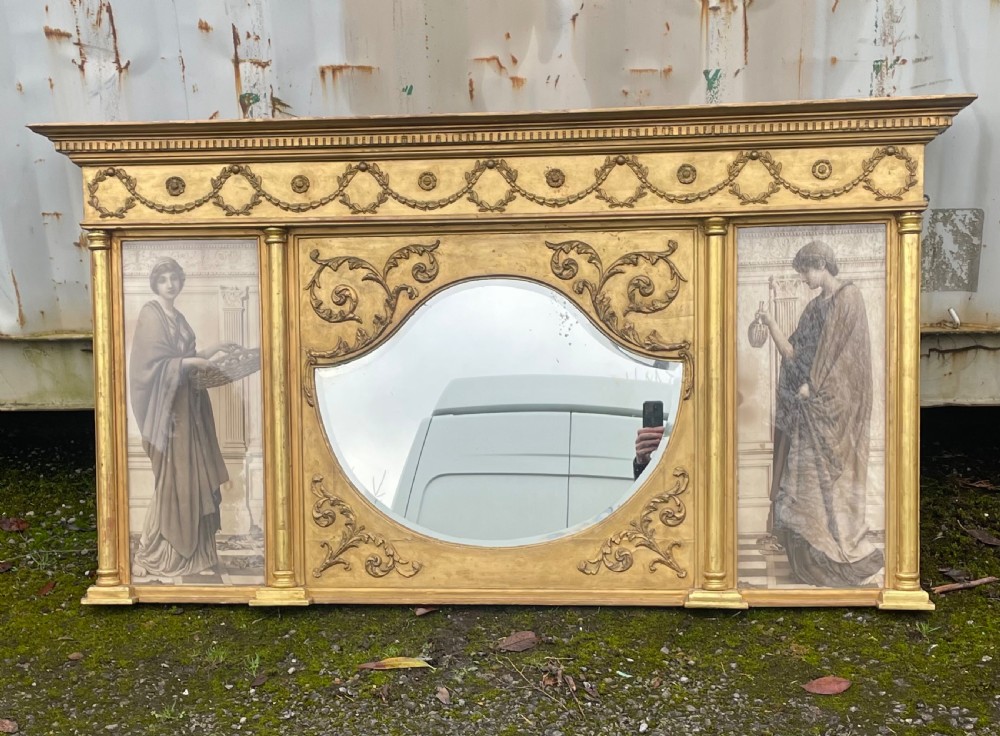 A wide Victorian giltwood overmantel mirror featuring a central shaped mirror plate flanked by classical female figures and decorated with festoon swags.