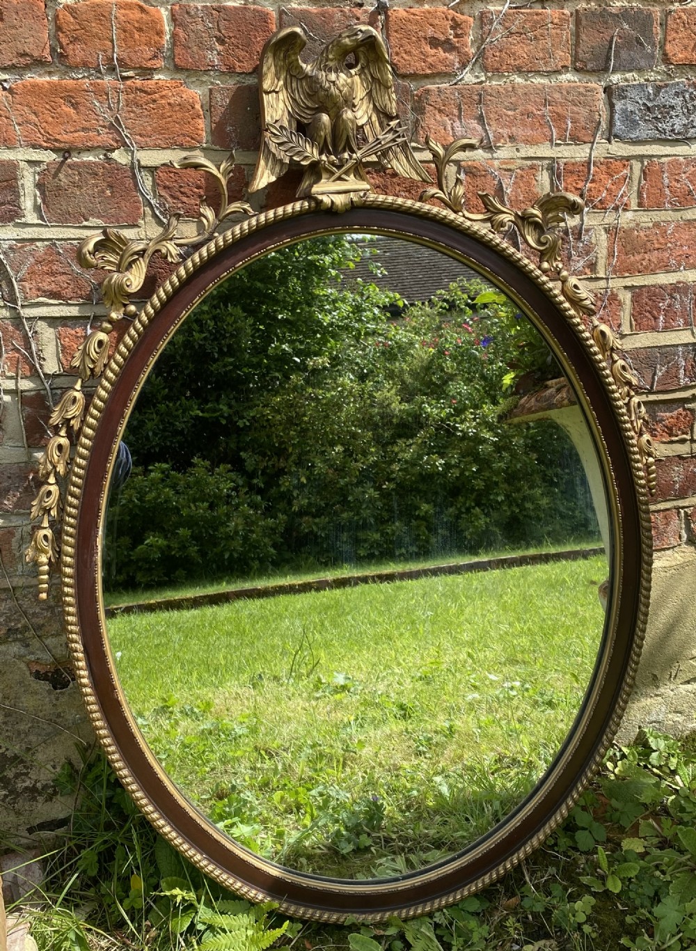 An oval mahogany wall mirror framed by a rope-twist border and surmounted by a carved giltwood eagle crest with foliate swags. View IV