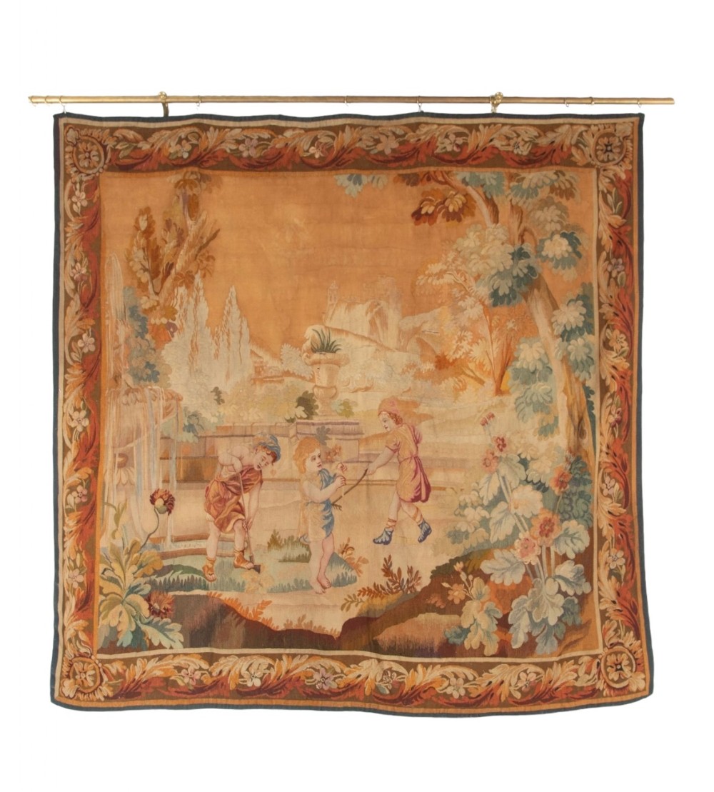 A 19th-century woven wall tapestry depicting three children playing in a classical garden setting with an ornamental floral border.
