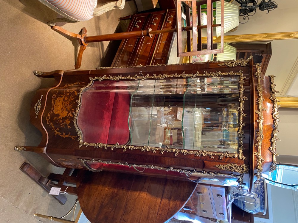 A French Rococo style serpentine glazed vitrine cabinet featuring dark wood veneer, intricate floral marquetry inlay on the lower panel, and decorative gilt bronze ormolu mounts. View IX