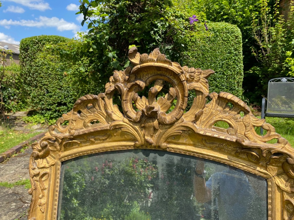 An eighteenth-century carved giltwood mirror featuring elaborate foliage cresting, ornate scrollwork frame, and an arched glass plate. View II