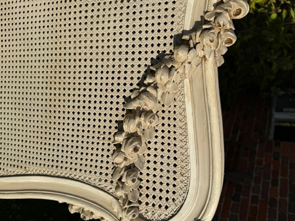A cream painted kingsize bed frame components featuring carved floral garlands, shell cresting, and woven rattan cane panels. View II