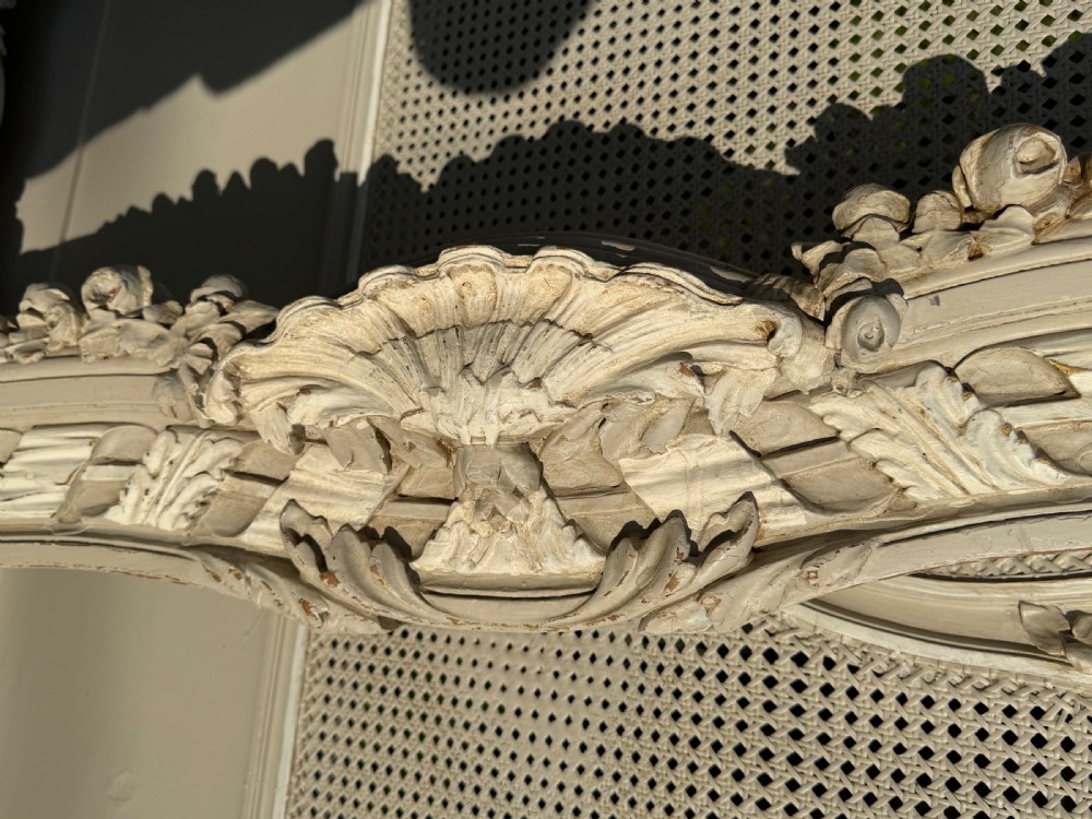 A cream painted kingsize bed frame components featuring carved floral garlands, shell cresting, and woven rattan cane panels. View III