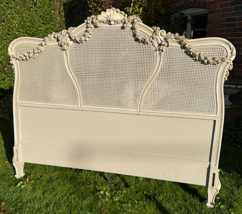 A cream painted kingsize bed frame components featuring carved floral garlands, shell cresting, and woven rattan cane panels. View V