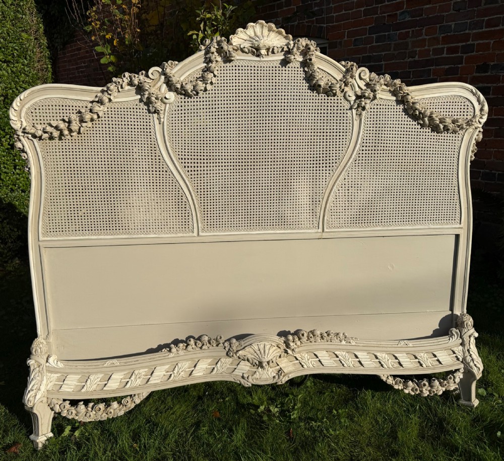 A cream painted kingsize bed frame components featuring carved floral garlands, shell cresting, and woven rattan cane panels. View VI