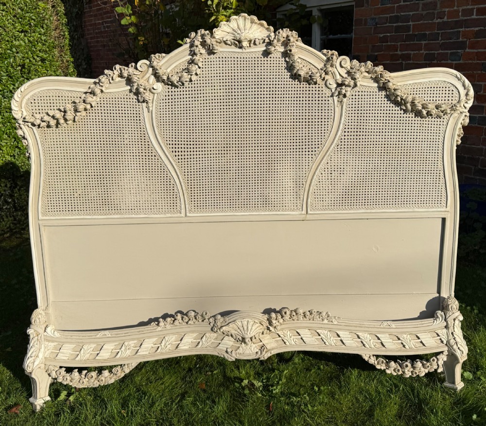 A cream painted kingsize bed frame components featuring carved floral garlands, shell cresting, and woven rattan cane panels. View VII
