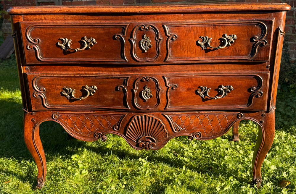 An 18th-century Rococo commode crafted from walnut, featuring two carved drawers with brass handles, cabriole legs, and a scallop shell carved into the lower apron.