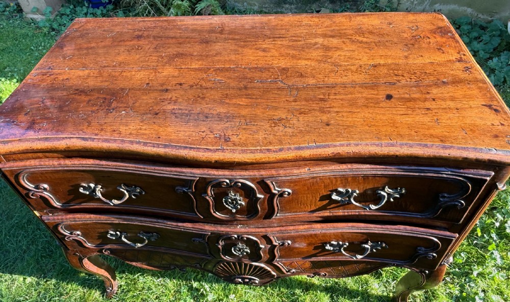 An 18th-century Rococo commode crafted from walnut, featuring two carved drawers with brass handles, cabriole legs, and a scallop shell carved into the lower apron. View V