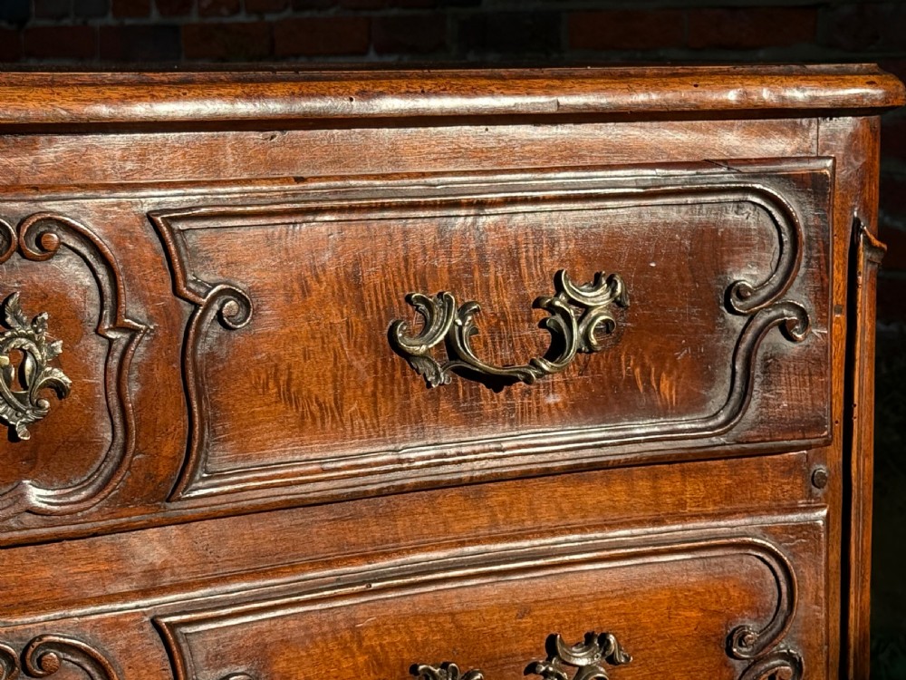 An 18th-century Rococo commode crafted from walnut, featuring two carved drawers with brass handles, cabriole legs, and a scallop shell carved into the lower apron. View VI