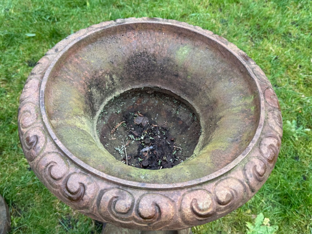 A pair of weathered rust-brown cast iron garden planters featuring cherub figures holding wide gadrooned urn bowls. View II