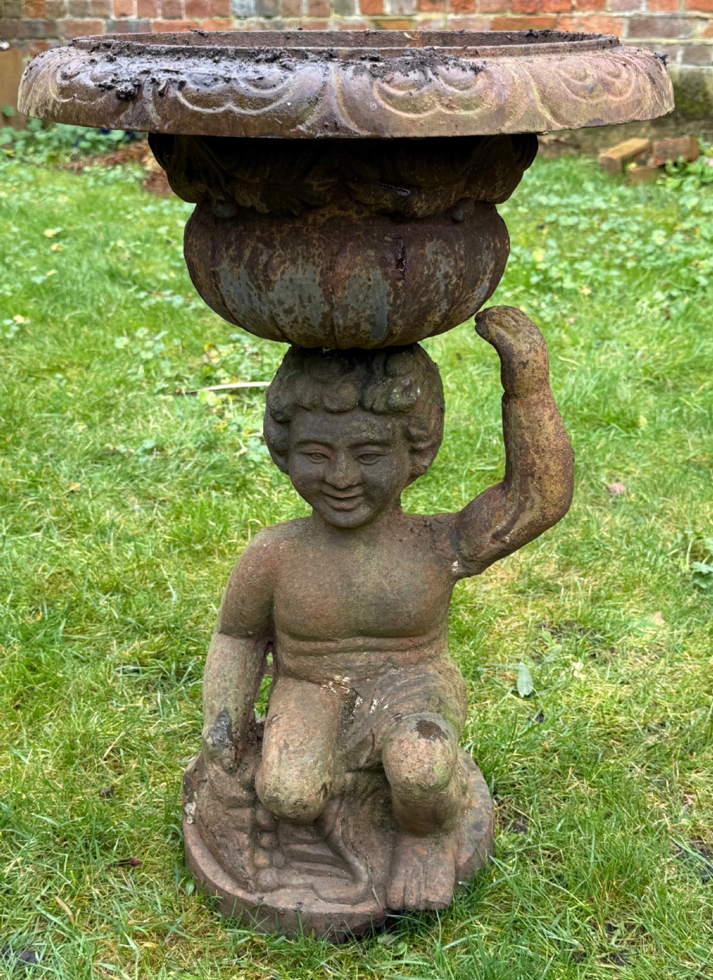 A pair of weathered rust-brown cast iron garden planters featuring cherub figures holding wide gadrooned urn bowls. View V