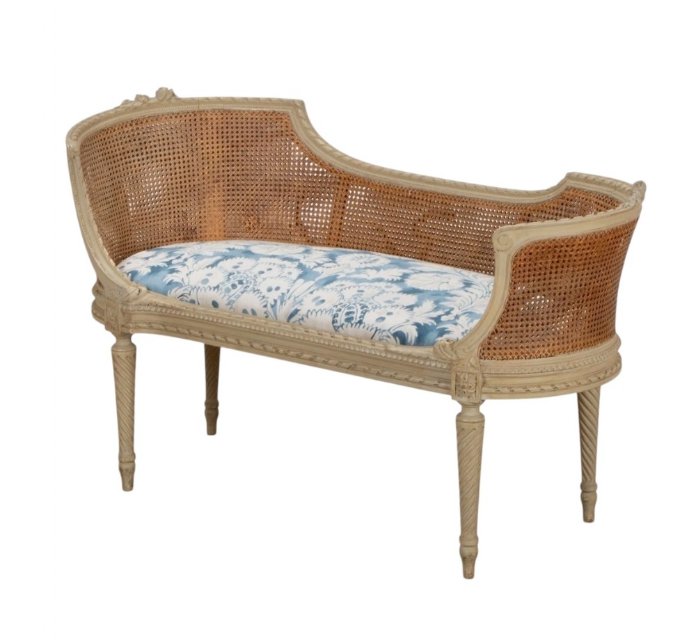 A French 19th-century style painted wooden settee with a curved caned backrest, fluted legs, and a blue and white patterned upholstered seat.