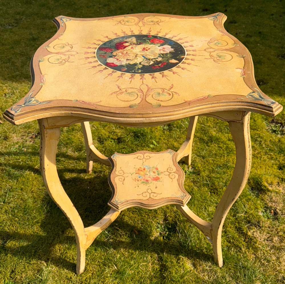 A cream-painted two-tier occasional table featuring cabriole legs, a shaped serpentine top with a floral central medallion, and decorative scrollwork borders. View III