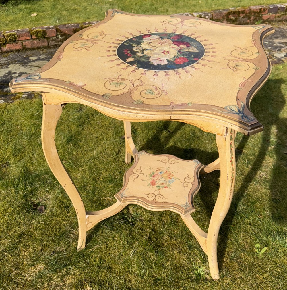 A cream-painted two-tier occasional table featuring cabriole legs, a shaped serpentine top with a floral central medallion, and decorative scrollwork borders. View V