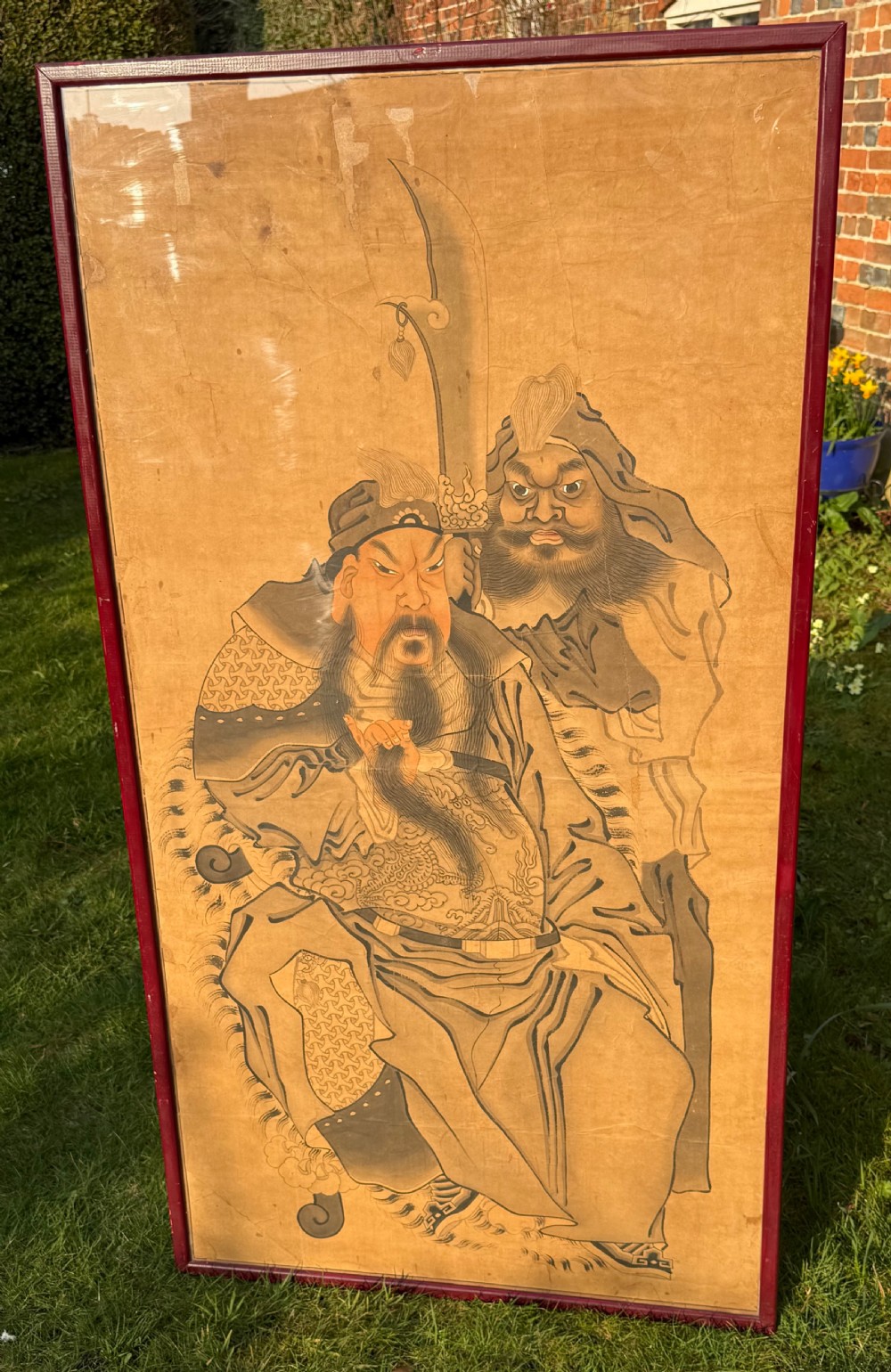 A large framed Chinese ink and watercolour painting depicting a seated bearded general accompanied by an attendant holding a crescent blade against an ochre background. View II