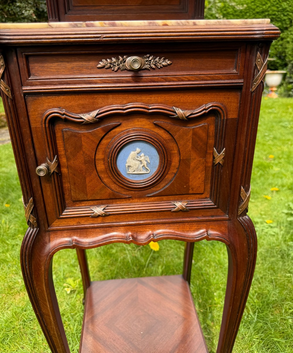 A pair of French Neoclassical wooden bedside tables featuring red marble tops, ceramic medallion inserts, Ormolu mounts, curved legs, and lower open shelves. View V