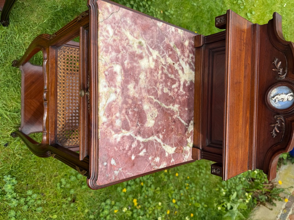 A pair of French Neoclassical wooden bedside tables featuring red marble tops, ceramic medallion inserts, Ormolu mounts, curved legs, and lower open shelves. View VI
