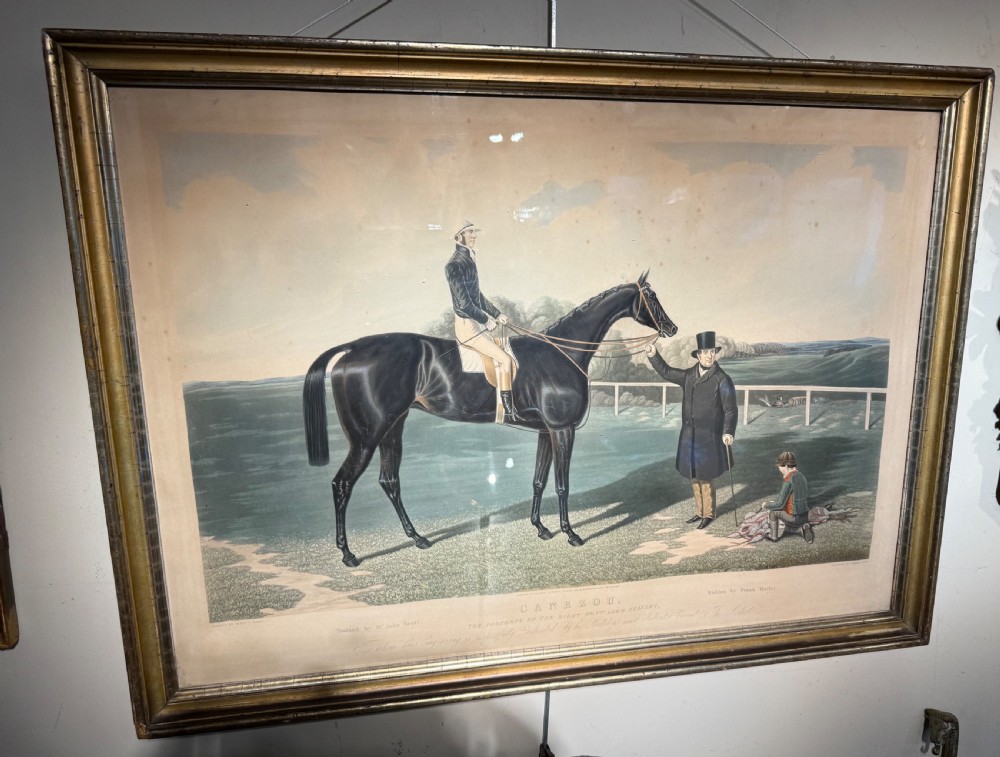 A 19th-century framed equestrian aquatint print depicting a dark racehorse with a jockey, accompanied by two figures in traditional attire set against a landscape. View III