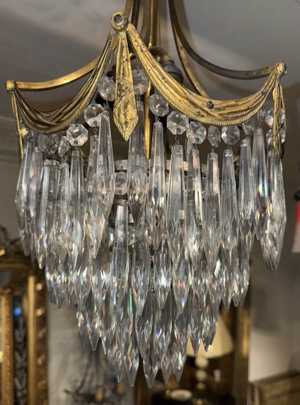An antique brass ceiling chandelier featuring a decorative gilded canopy, curved frame, and cascading tiers of pointed cut glass drops. View VI