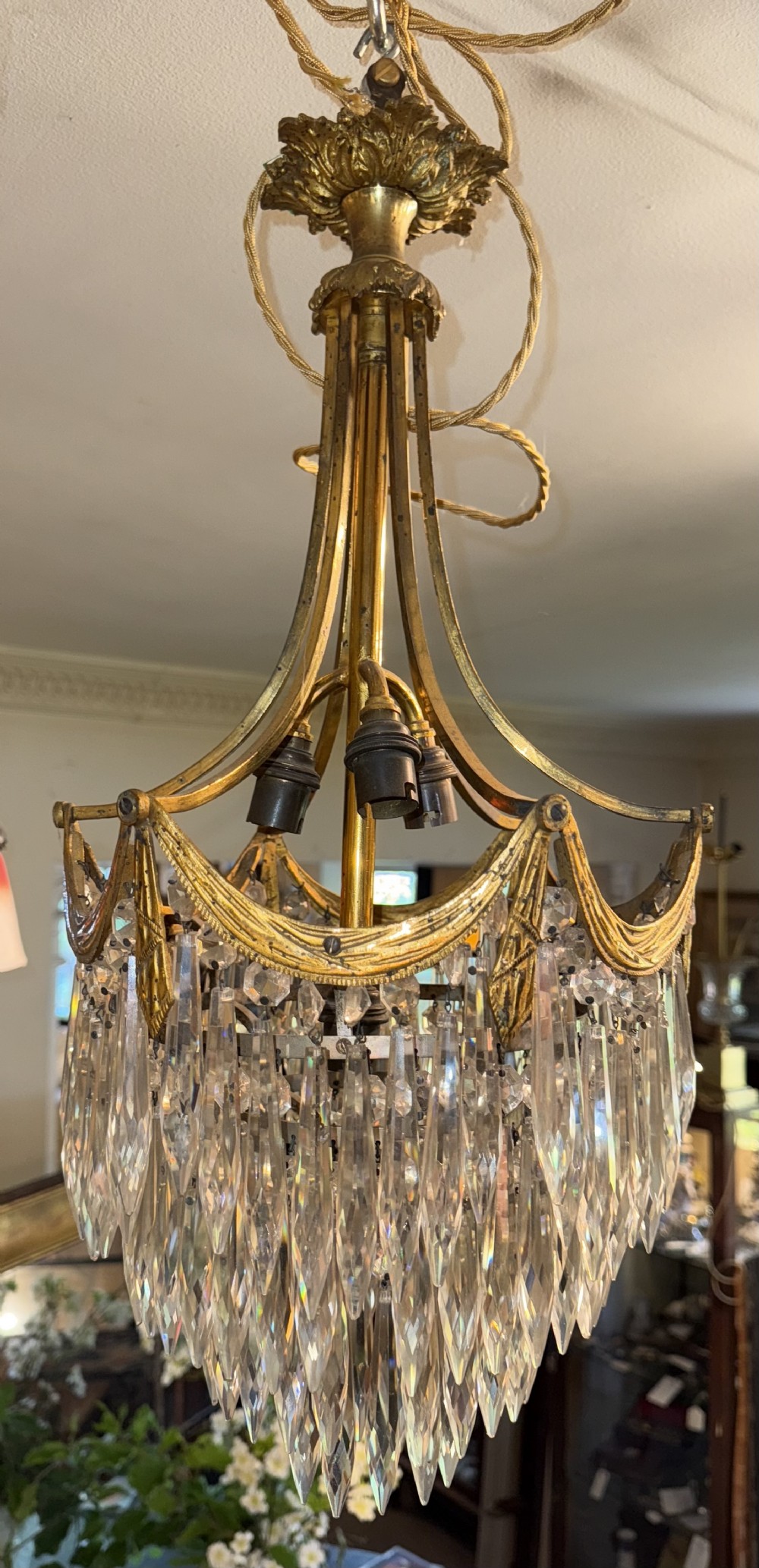 An antique brass ceiling chandelier featuring a decorative gilded canopy, curved frame, and cascading tiers of pointed cut glass drops.