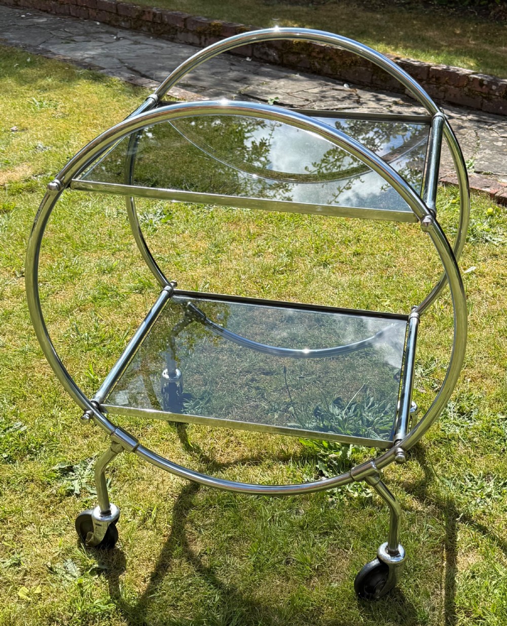 An Art Deco circular chrome frame drinks trolley with two rectangular smoked glass shelves set on castor wheels. View II