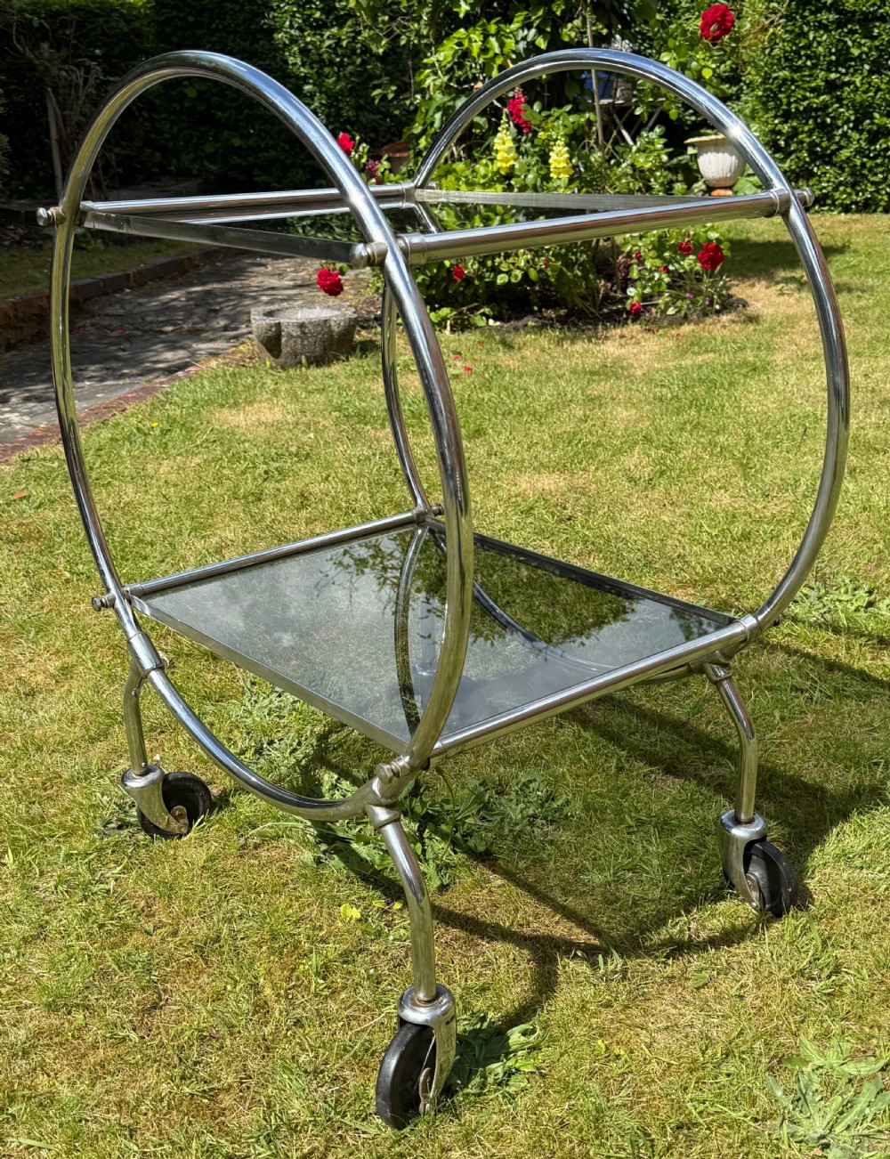 An Art Deco circular chrome frame drinks trolley with two rectangular smoked glass shelves set on castor wheels. View III