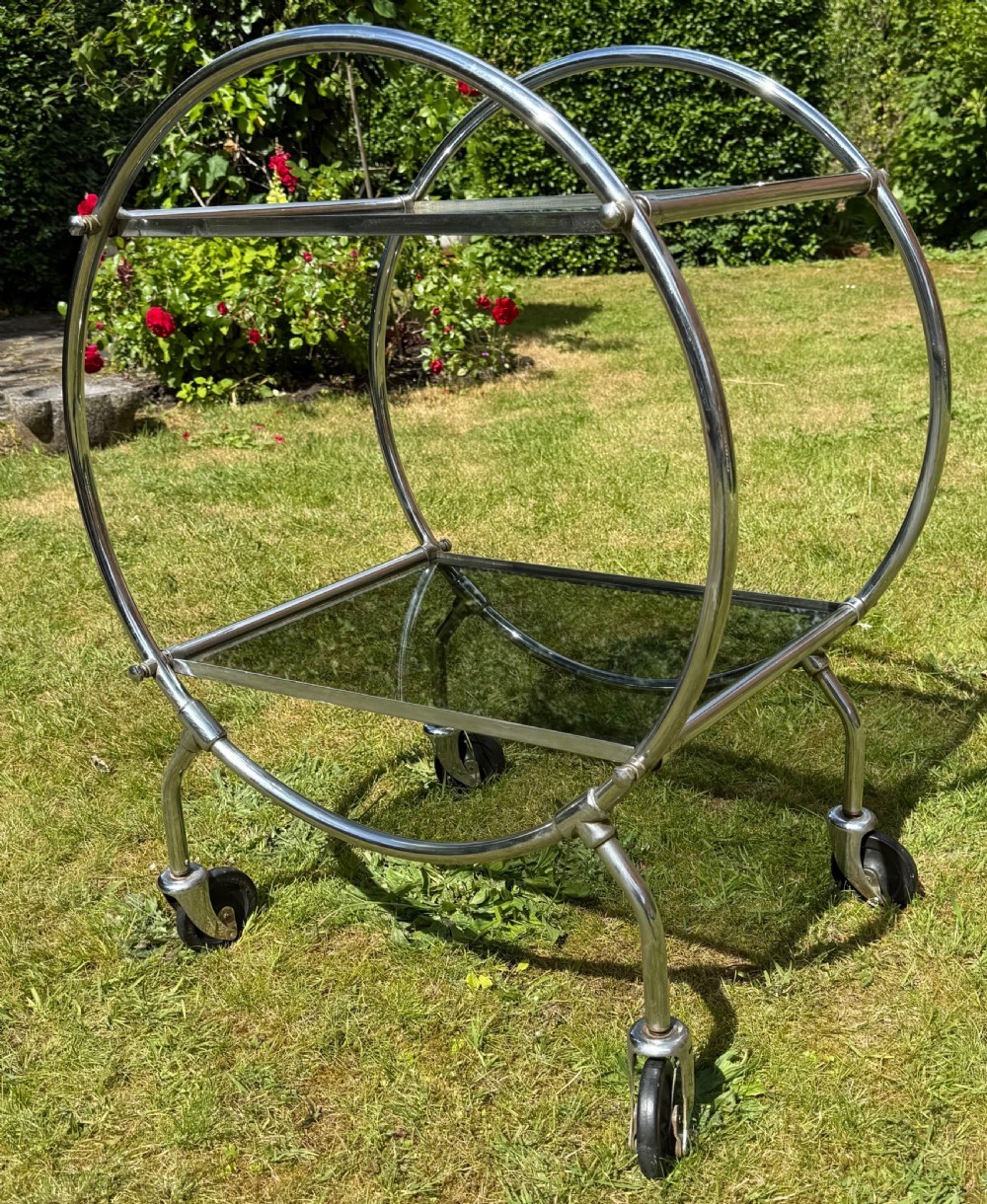 An Art Deco circular chrome frame drinks trolley with two rectangular smoked glass shelves set on castor wheels. View IV