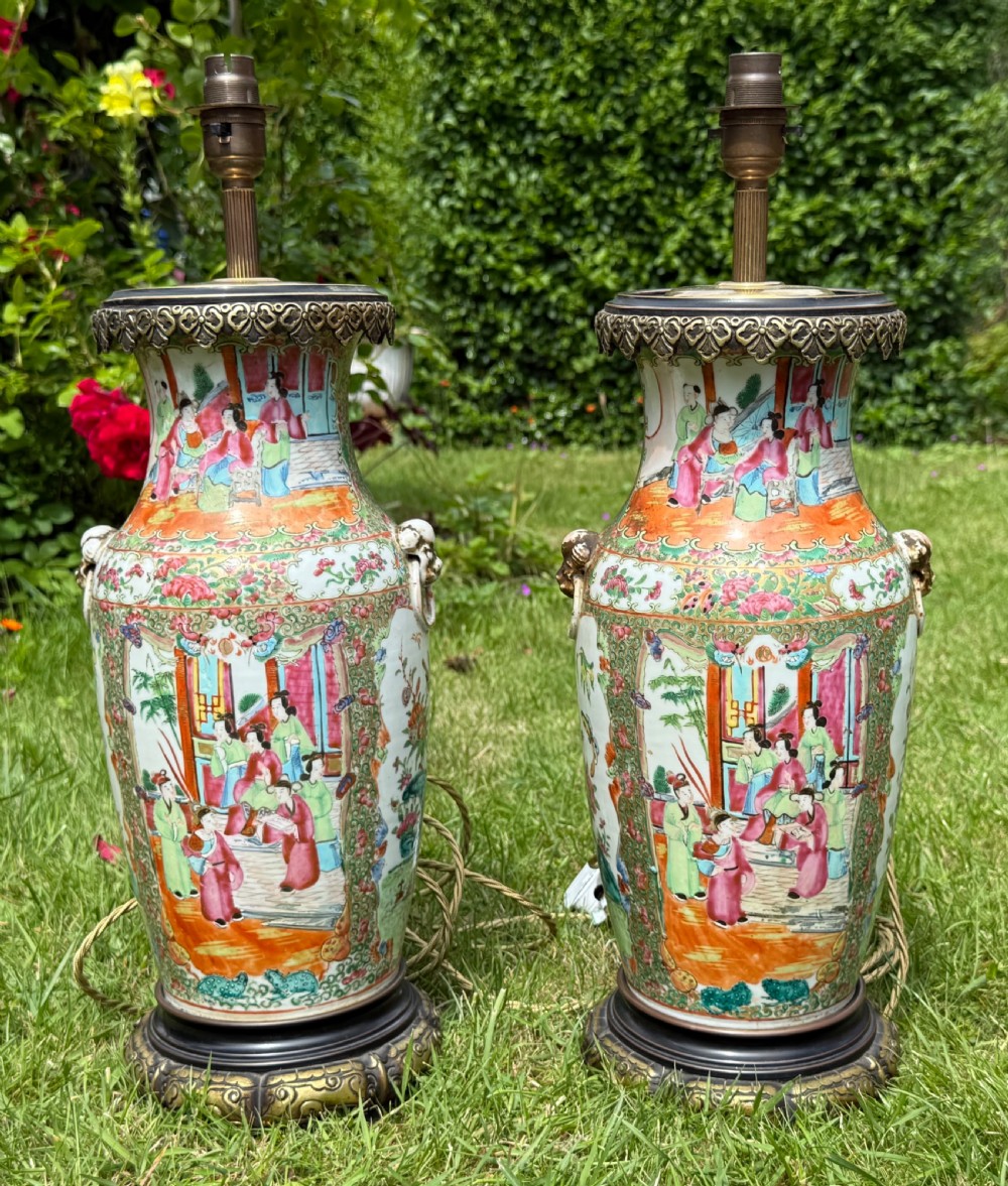 A pair of 19th-century Chinese Famille Rose porcelain vase lamps featuring detailed hand-painted figural scenes, brass mounts, and carved dark wood bases.