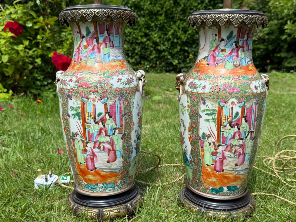A pair of 19th-century Chinese Famille Rose porcelain vase lamps featuring detailed hand-painted figural scenes, brass mounts, and carved dark wood bases. View II