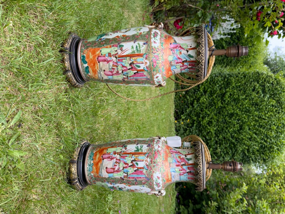 A pair of 19th-century Chinese Famille Rose porcelain vase lamps featuring detailed hand-painted figural scenes, brass mounts, and carved dark wood bases. View VI