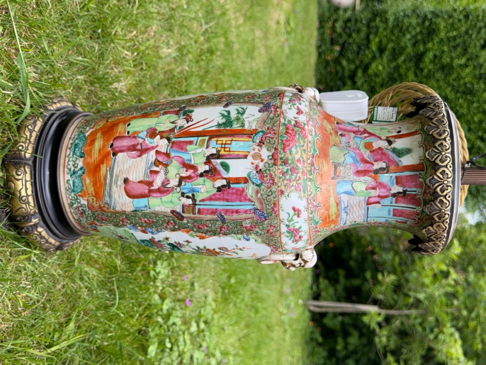 A pair of 19th-century Chinese Famille Rose porcelain vase lamps featuring detailed hand-painted figural scenes, brass mounts, and carved dark wood bases. View VII