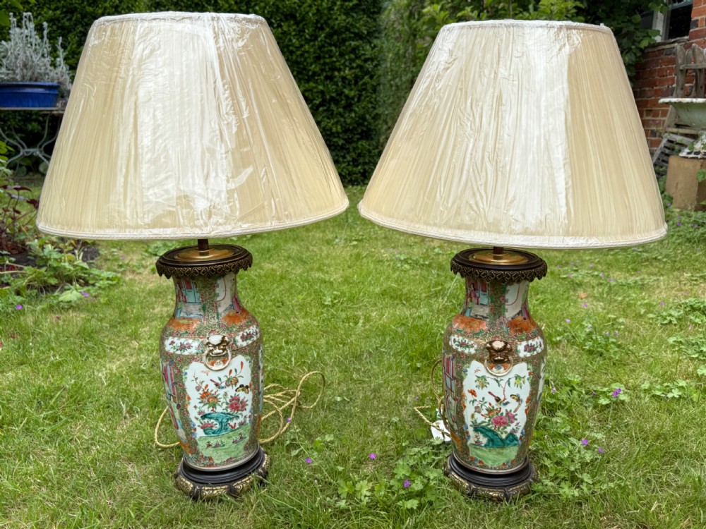 A pair of 19th-century Chinese Famille Rose porcelain vase lamps featuring detailed hand-painted figural scenes, brass mounts, and carved dark wood bases. View IX