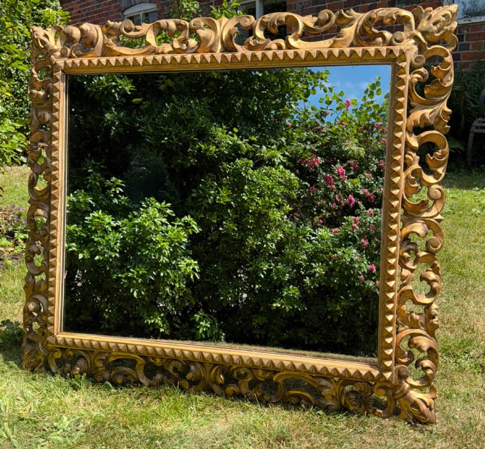 A large rectangular wall mirror featuring an intricate hand-carved gold giltwood frame with openwork acanthus foliage and a notched inner border.