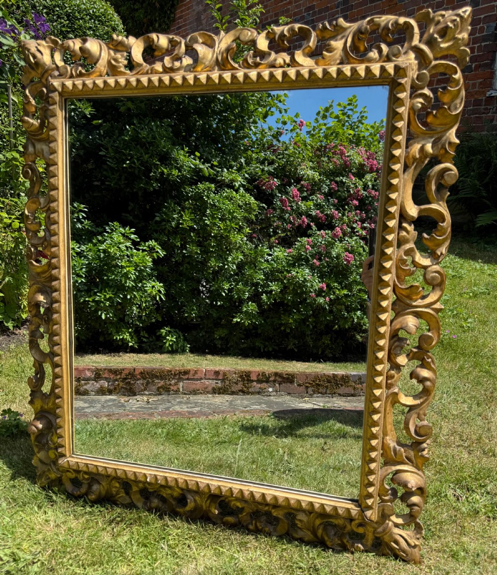 A large rectangular wall mirror featuring an intricate hand-carved gold giltwood frame with openwork acanthus foliage and a notched inner border. View VIII