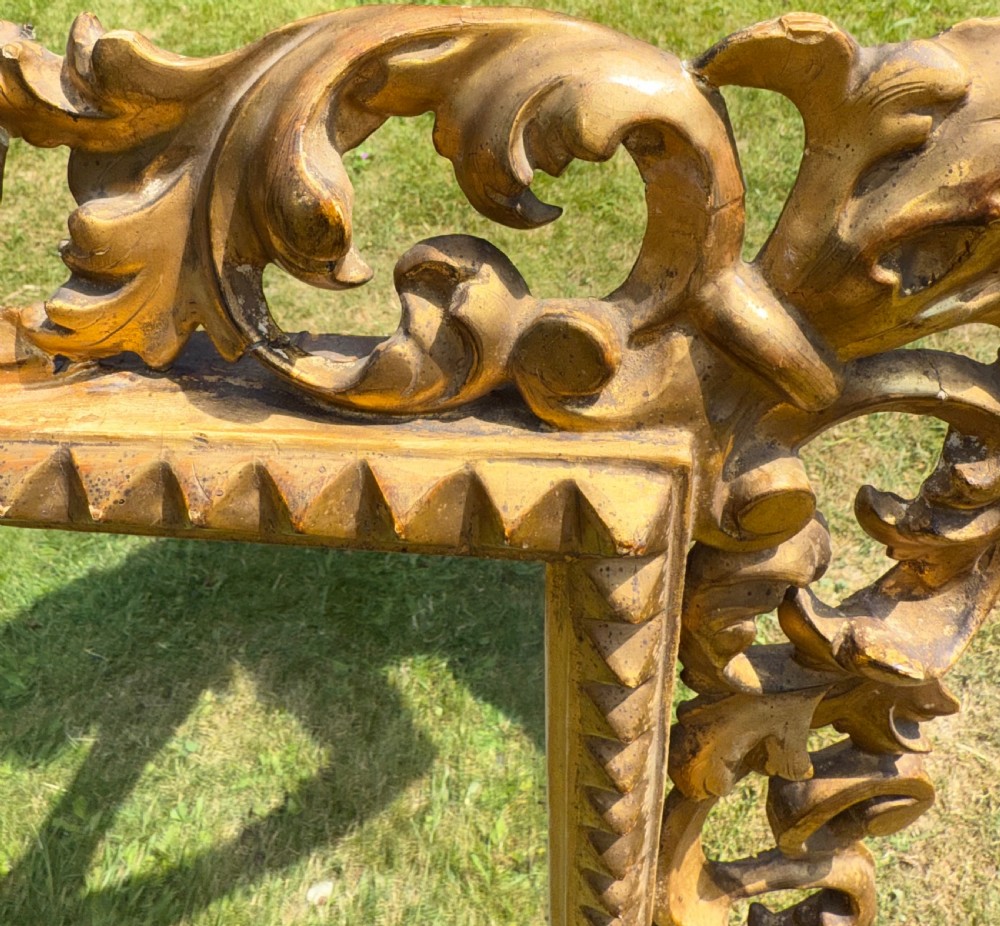 A large rectangular wall mirror featuring an intricate hand-carved gold giltwood frame with openwork acanthus foliage and a notched inner border. View IX